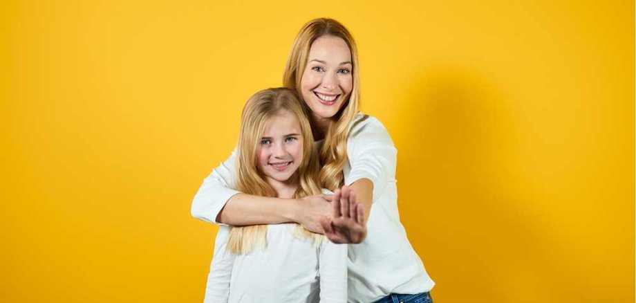 Eine Mutter umarmt Ihre Tochter vor einem gelben Hintergrund